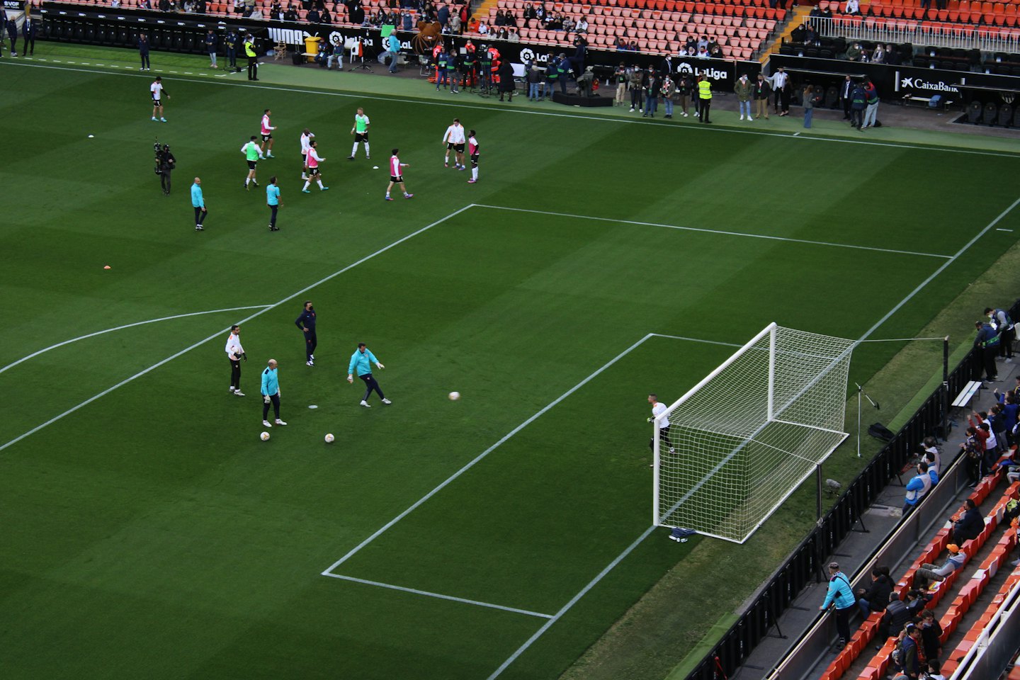 Piłkarze trenują na zielonej murawie stadionu obok bramki.